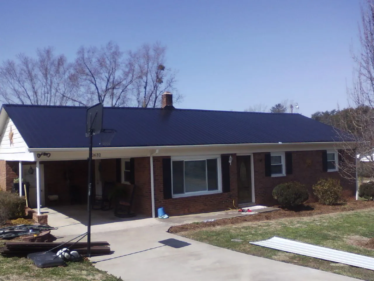 Finished dark blue metal roof on a brick ranch with a carport in Boone Grove