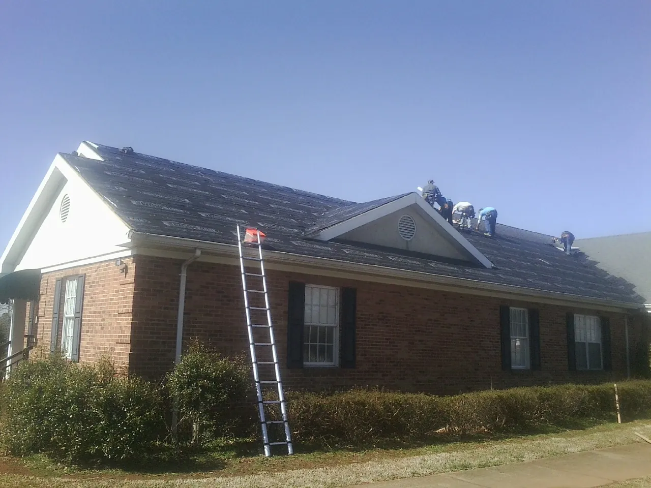 Crew tearing shingles off a brick ranch roof with a ladder set — Emergency Roof Repair work by our crew in Boone Grove