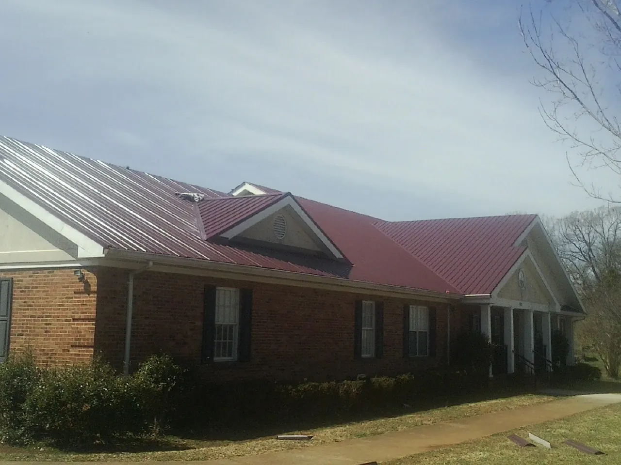 Red metal roof with gabled entries on a long brick building, from a Hail Damage Roof Repair job in Boone Grove