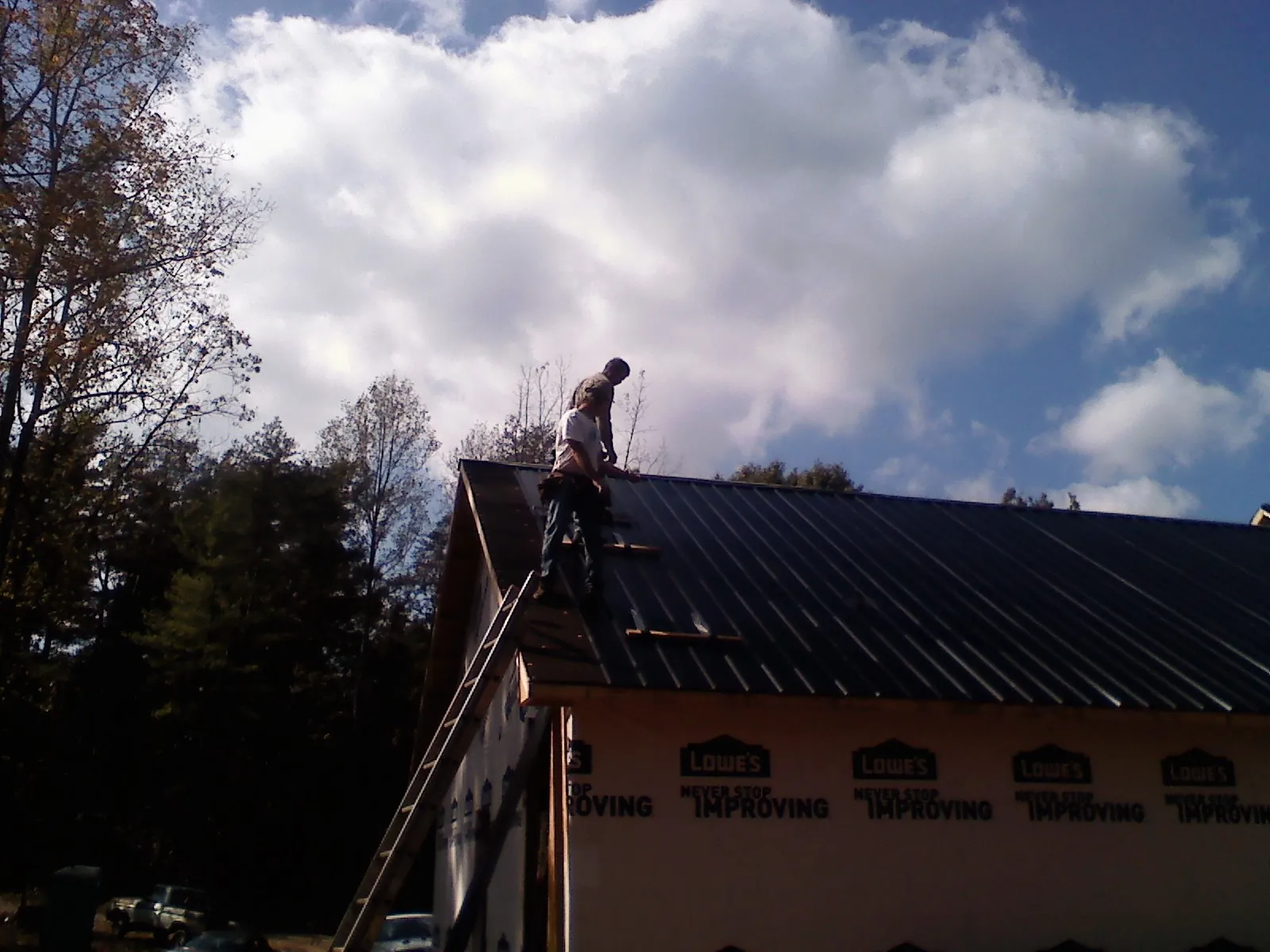 Roofer fastening dark metal panels high against a cloudy sky, from a Roof Inspection job in Boone Grove