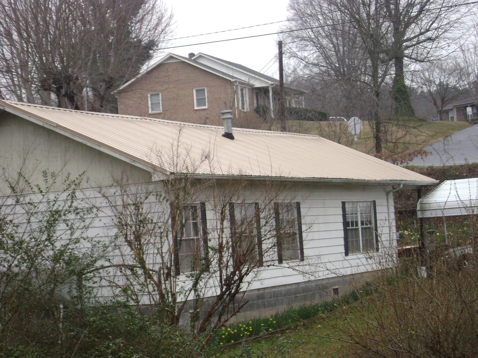 Tan metal roof on a white sided house set into a hillside — Commercial Roofing by Roofing Brothers in Boone Grove