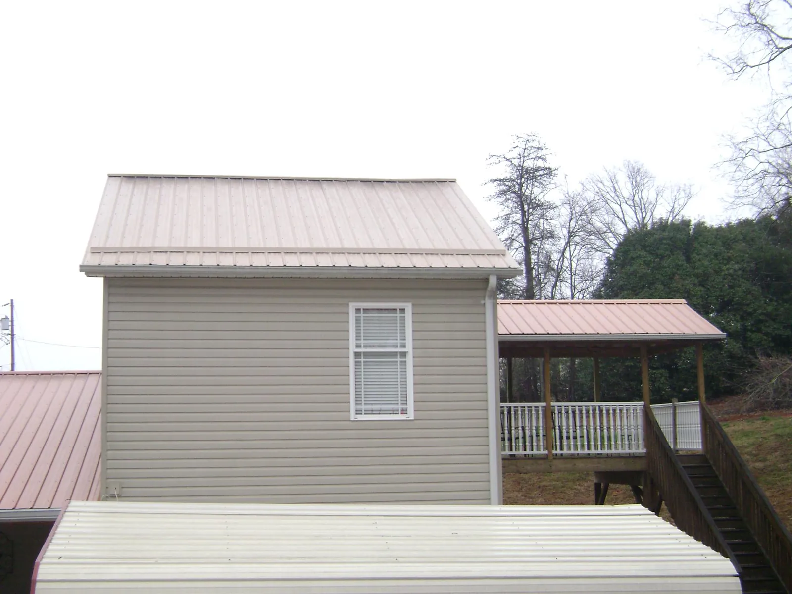 Tan metal roofs on a two story addition and attached porch, from a Roof Replacement job in Boone Grove